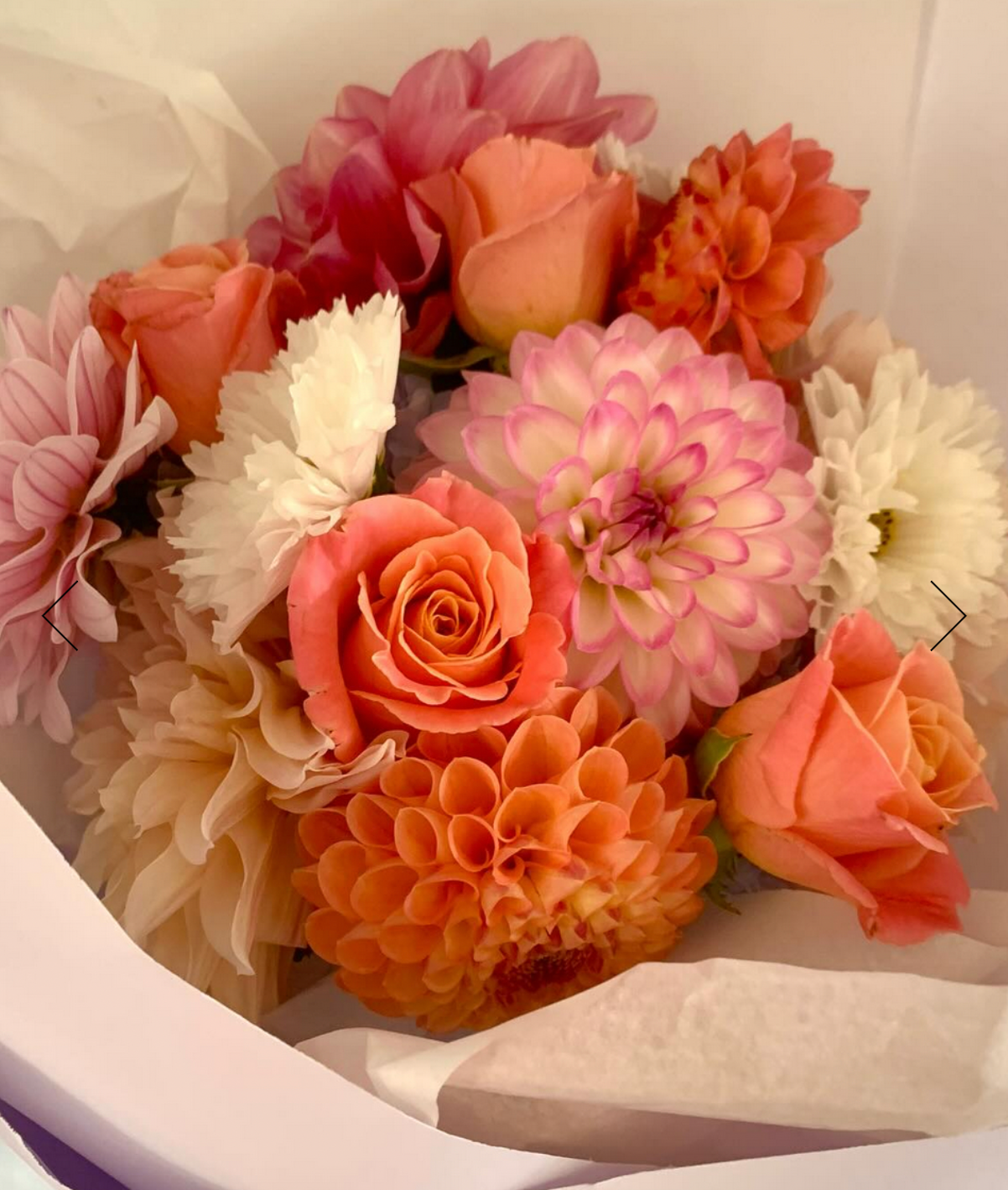 Pastel Posie bouquet made with seasonal soft pink, orange and white flowers, wrapped in white tissue paper.