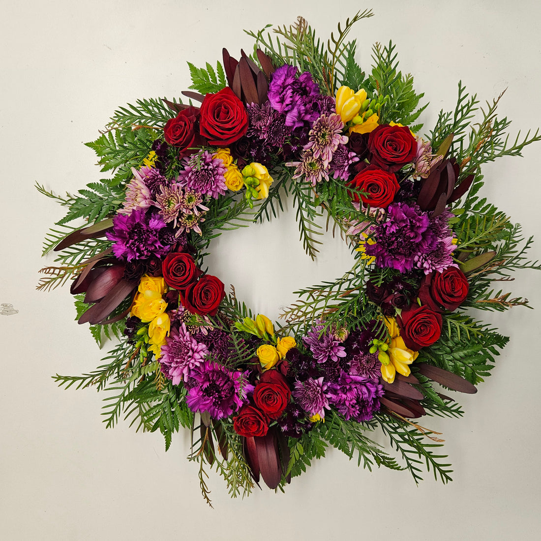 A bright floral tribute wreath with red, purple and yellow flowers with greenery.