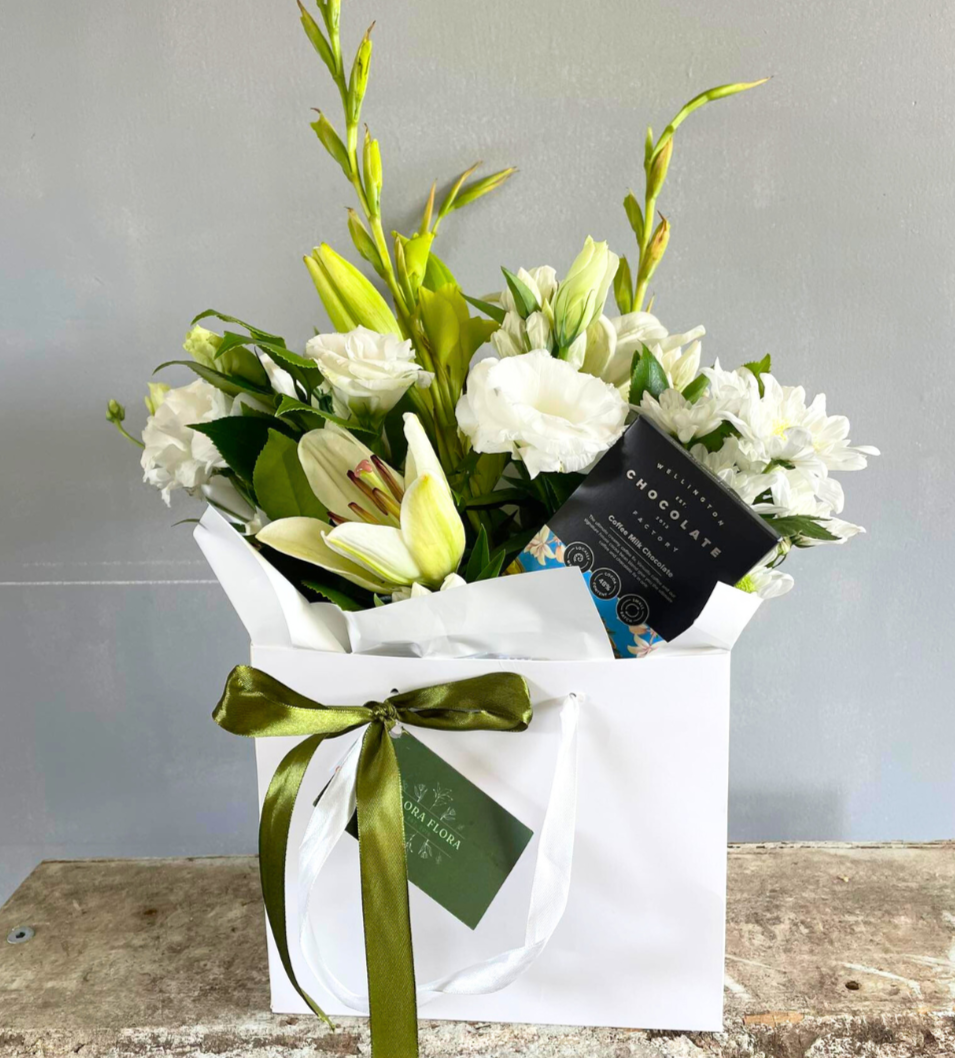 Bright White &amp; Chocs gift basket with white flowers and Coffee Milk Chocolate from Wellington Chocolate Factory, presented in a white gift bag tied with green ribbon.