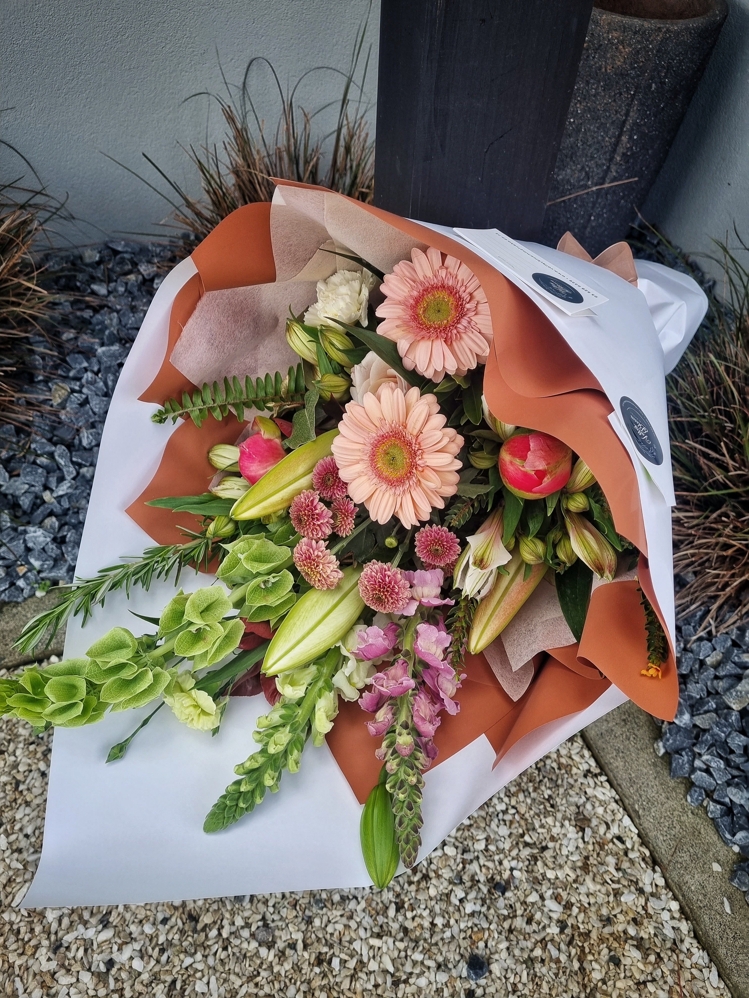 Rustic Bouquet with soft warm-toned flowers with foliage, wrapped in orange and white tissue paper.