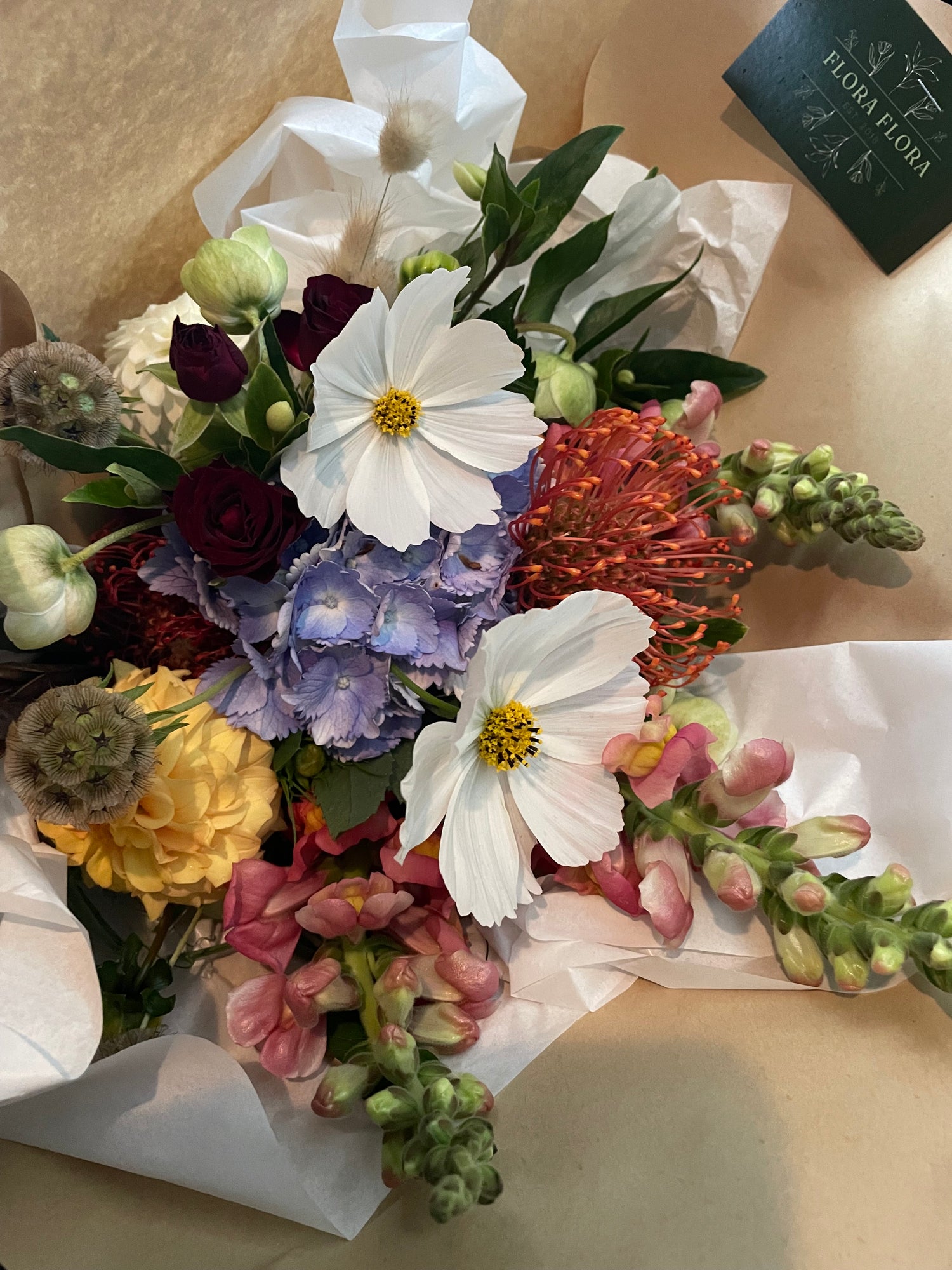 An example of what your Seasonal Bunch from Flora Flora could look like. Multi-coloured flowers with greenery, wrapped in brown kraft paper.