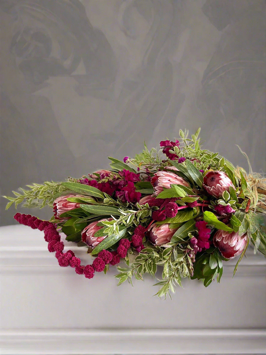 Wild Funeral Casket Sheaf with rich pink flowers and soft greenery laid atop a casket.
